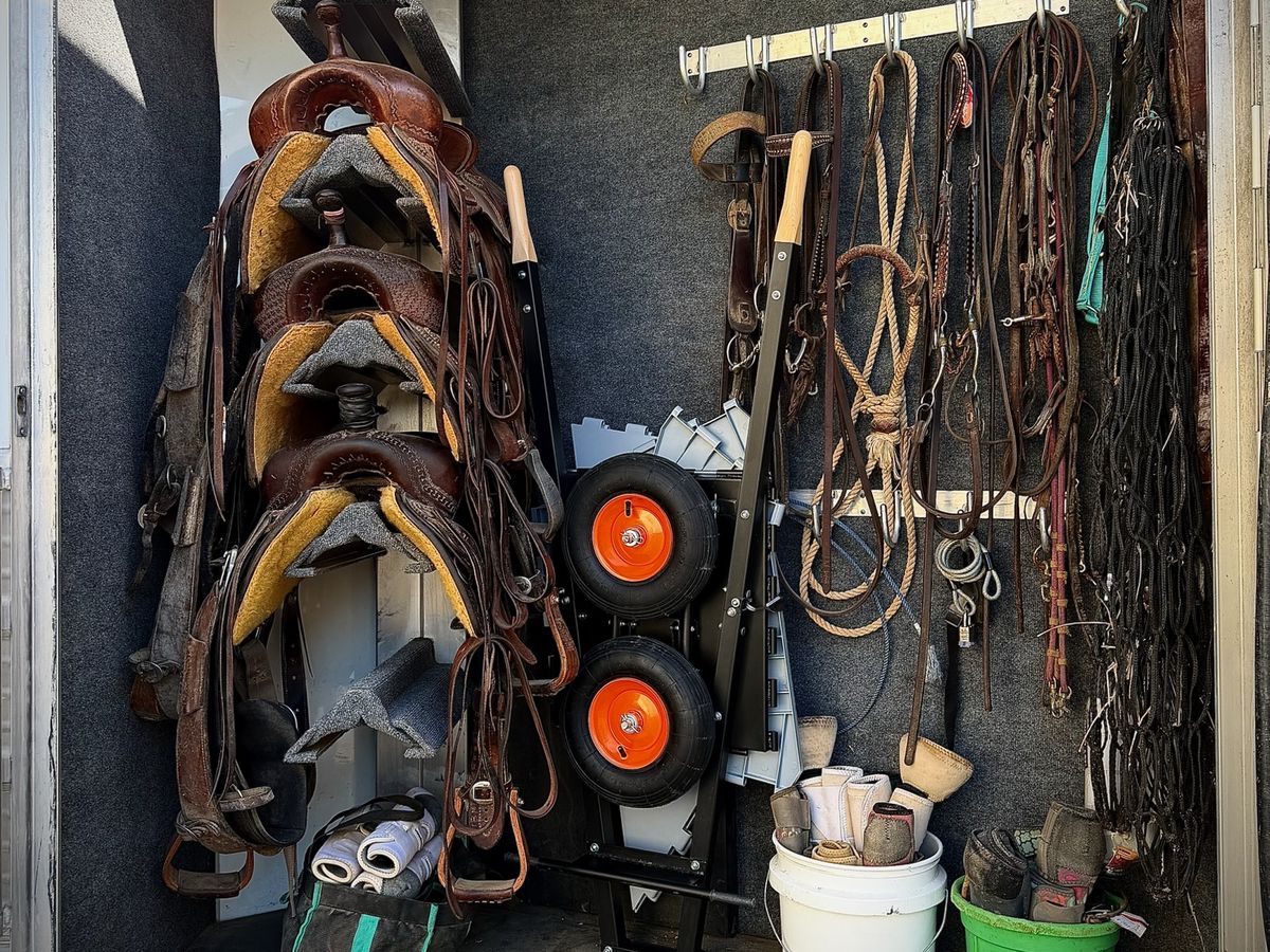 The collapsed wheelbarrow stood on end in the back tack of a horse trailer, beside the saddles
