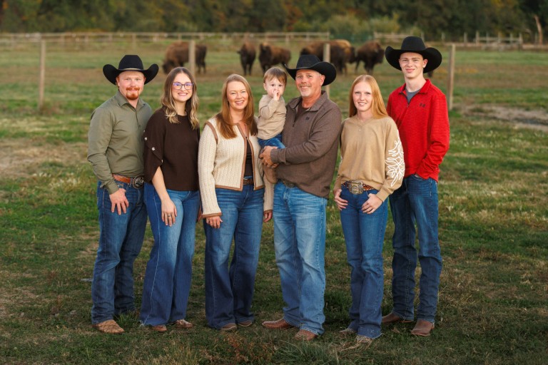 The family standing together in a pasture, bison grazing behind them