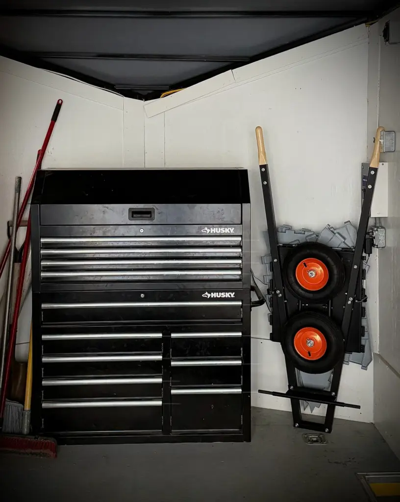 Collapsed and hung on a garage wall beside a rolling tool chest, wheels pinned on the storage rods