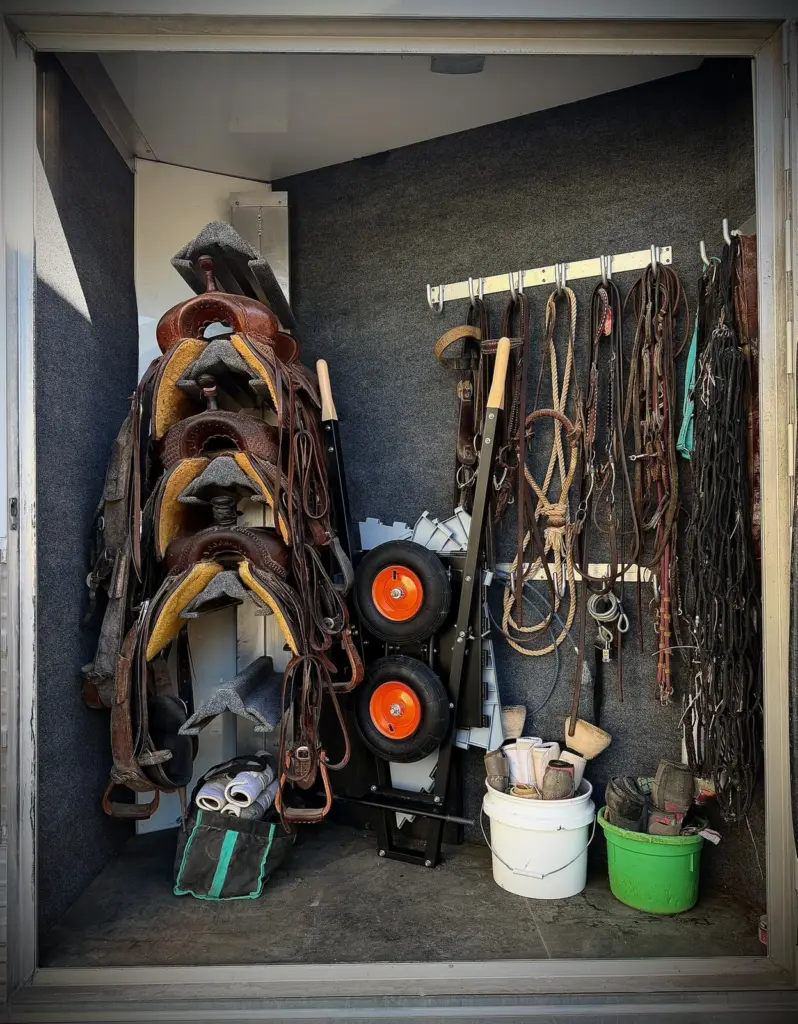 The Workin' Collapsible Wheelbarrow collapsed and stood on end in a horse trailer back tack, beside the saddles and bridles