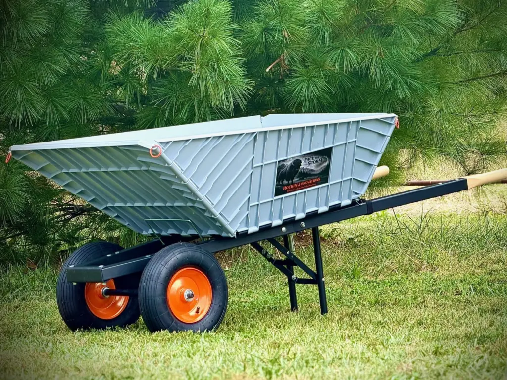 The Workin' Collapsible Wheelbarrow assembled, three-quarter view: gray poly tub, black steel frame, wood-grip handles, orange-rimmed wheels