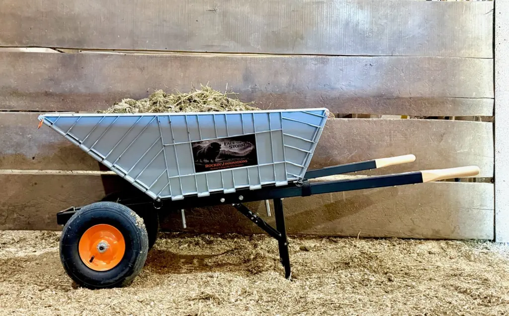 The wheelbarrow loaded with hay in a horse stall, bedding underfoot