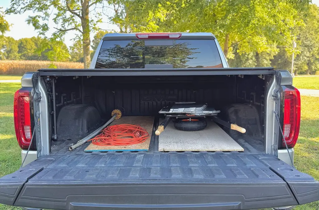 Collapsed and lying flat in a pickup bed with the tailgate down, beside an extension cord and a board